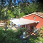 petite maison rouge avec forêt, store sur terrasse vue de coté