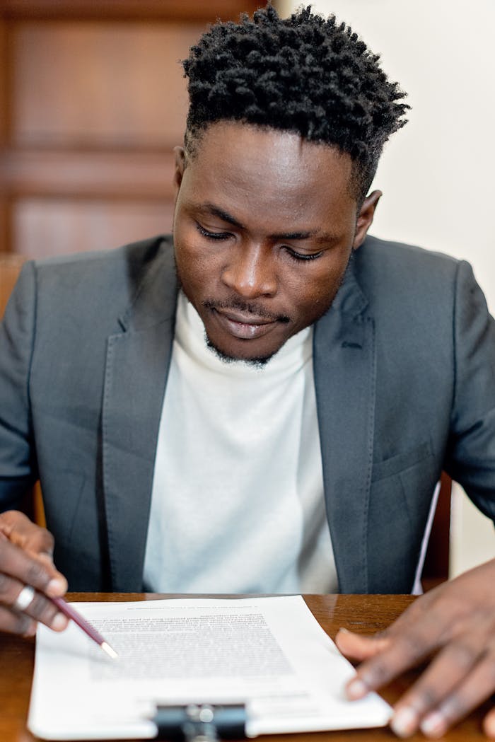 our-story-01 A focused businessman in a gray suit closely reviewing legal paperwork at a desk indoors.